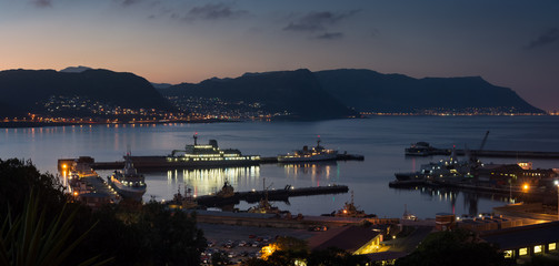 The lights on a ship in harbour reflect in the calm water at sunset