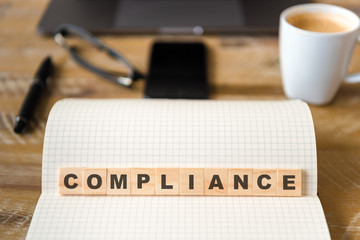 Closeup on notebook over wood table background, focus on wooden blocks with letters making Compliance text