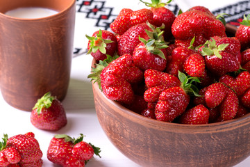 A cup with fresh homemade strawberries and mug  of milk  stand on a wooden white  table with a ornament napkin