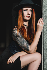 Creative redhead woman in gothic black dress and hat in the city. Street style