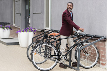 trendy african american businessman with bike on parking for bicycles