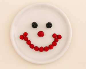 Gesicht aus Himbeeren und Brombeeren auf einem weissen Teller
