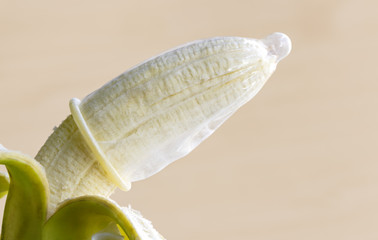Condom and banana on the brown background.