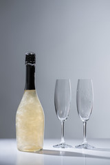 close up view of bottle of champagne and empty glasses on grey background