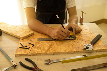 Close-up of male carpenter hands drawing mark on wooden flooring with steel ruler and pencil.