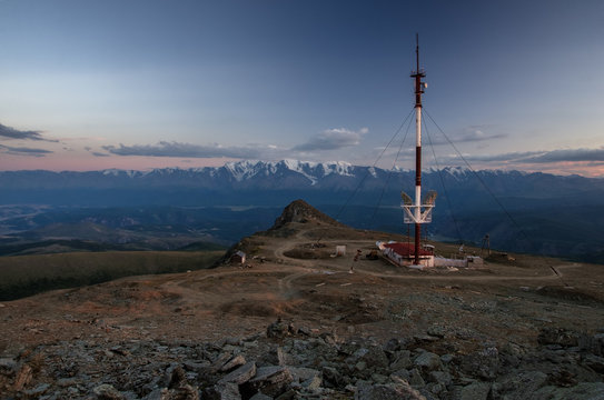 Dramatic dark twilight peak with communication construction tower on a highland mountain plateau with ranges of snow peaks at storm sunset ilumination Kurai Altai Mountains Siberia Russia