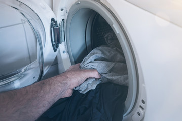 close-up of male hand putting dirty laundry in drum of washing machine