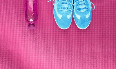 Light blue sneakers and water bottle on pink background of yoga mat. Concept of healthy lifestile. Flat lay, top view, copy space 