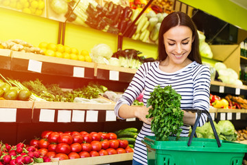 Attractive smiling young girl in casual clothes selects fruits and vegetables from a shelf in a grocery store.