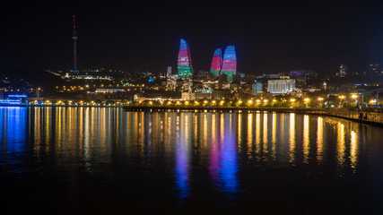 Fototapeta na wymiar Baku night cityscape with flaming towers and reflections in the Caspian sea bay