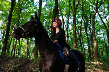 Mystical girl in wreath wear in black at horse in wood.