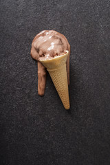 Dropped and melting chocolate ice cream cone on pavement in summer heat