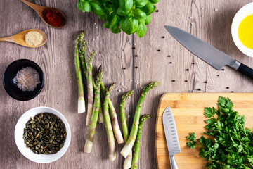 parsley, asparagus, olive, pumpkin seeds, basil red salt, yeast flakes and red peper on the wooden spoons, kitchen knives, wooden background
