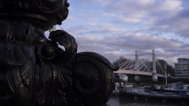 Timelapse of Albert Bridge with boats moored in Thames River, bronze sculpture in foreground, Chelsea, London, United Kingdom