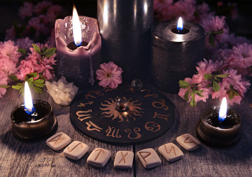 Runes, black candles and zodiac circle against the background with sakura flowers. Occult, esoteric and divination still life. Halloween background with vintage objects