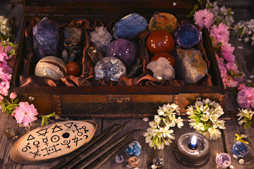 Box with magic crystals and stones, black candle and spring flowers. Occult, esoteric and divination still life. Halloween background with vintage objects 