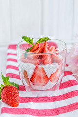Chia pudding with fresh strawberries and mint in glass on striped background. Concept of healthy eating
