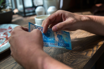 Man holds New 2000 rubles banknote in  hand in cafe.