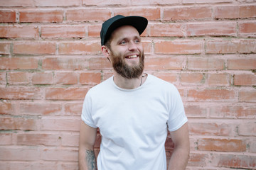 Hipster handsome male model with beard wearing white blank t-shirt and a baseball cap with space for your logo or design in casual urban style