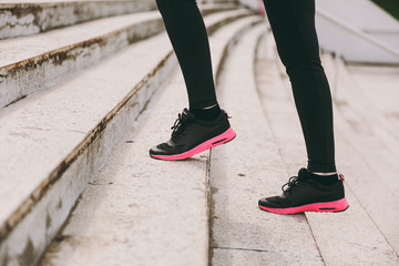 Cropped photo close up of female legs in sportswear, black and pink woman sneakers doing sport exercises, climbing on stairs outdoors. Fitness, healthy lifestyle concept. Copy space for advertisement.