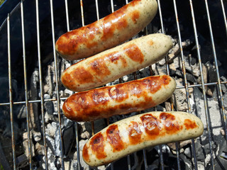 Würstchen auf einem Grillrost eines Holzkohlegrills bei einer Gartenparty