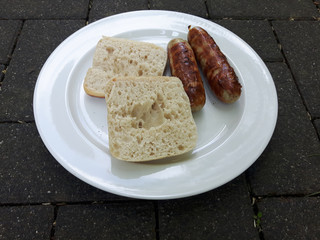 2 Würstchen vom Grill und ein aufgeschnittenes Brötchen auf einem Teller