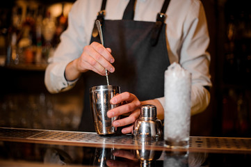 Fototapeta na wymiar Bartender stirring an alcoholic drink in the steel shaker