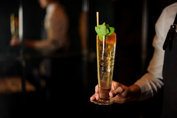 Professional bartender holding a summer orange cocktail with mint