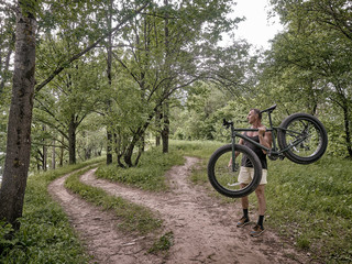 A trained man is riding a fat bike along forest paths.