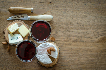 Two glass of red wine with few pieces of cheese and knives at wooden background. top view