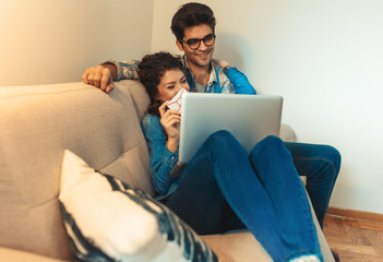 Smiling young couple sitting on sofa at home enjoying together, shopping online over the laptop.