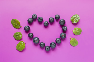 Blueberries laid out in the shape of a heart with mint leaves on bright crimson background