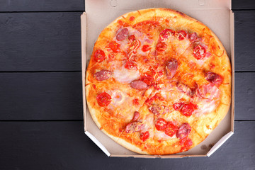 Pizza on a black wooden background, Italian pizza with tomatoes, bacon, sausages and cheese, fast food, festive food on a dark background, copy space, American cuisine