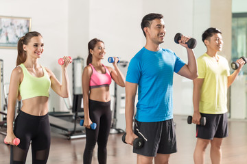 Fototapeta premium Fit handsome man smiling while exercising alternate bicep curls with dumbbells during group workout class in a modern fitness club