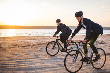 Obraz premium Two young men riding bicycles on the beach on the background of an orange sunsetting sky