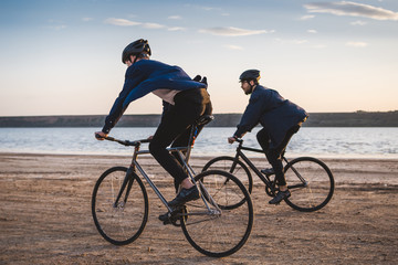 Two young men riding bicycles on the beach on the background of an orange sunsetting sky