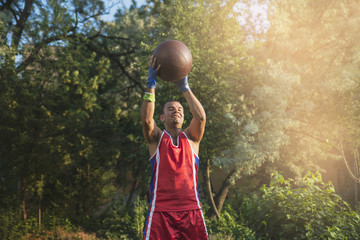 Young athlete performs sports exercises with a ball outdoors.