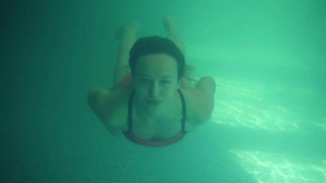 Young beautiful woman swimming in the pool under water. Gorgeous front view. Blue and green water. Smilling