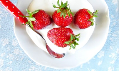 fresh strawberries in sour cream on white plate with spoon. close-up. delicious dessert