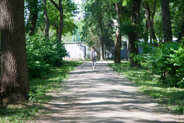 Blurred image of people walking in the park. A woman is walking with a dog. A child is riding a bicycle