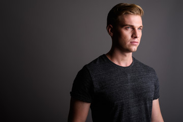 Fototapeta premium Young handsome man with blond hair wearing gray shirt against gr