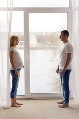 pregnant girl standing with her husband next to the window