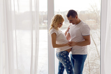 pregnant girl standing with her husband next to the window