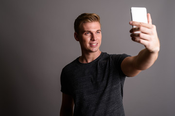 Young handsome man with blond hair wearing gray shirt against gr