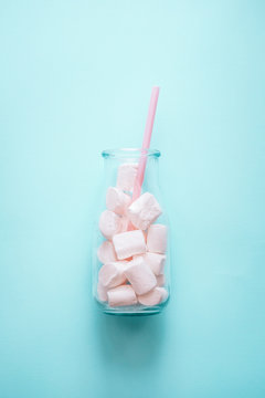 Creative minimalism still life on pastel blue colored background. Glass bottle with marshmallows and pink straw. Copyspace 