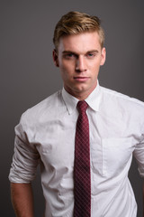 Young handsome businessman with blond hair against gray backgrou