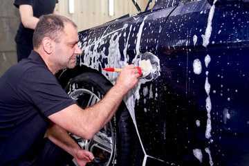 A man washes a blue car. Thorough washing of the body with foam and a high-pressure apparatus