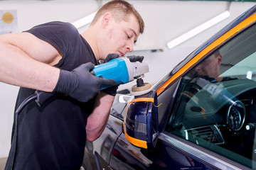 A man is polishing a blue car. Polishing machine and polishing paste for gloss.