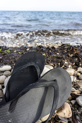 Chanclas  de verano de goma negra sobre cantos ovalados frente al mar
