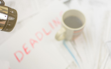 Deadline written on paper and a cup of coffee on scattered papers. Toned.